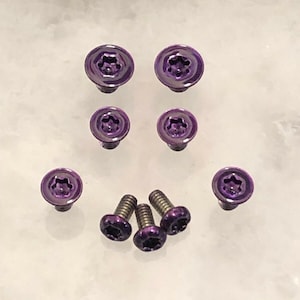 Peut inclure: Un ensemble de huit vis violettes à tête étoilée. Les vis sont disposées en motif sur une surface blanche.