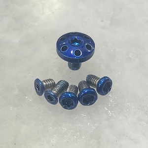 Könnte beinhalten: Ein Satz von sechs blauen Schrauben mit einem Sternkopf. Die Schrauben sind in einem Kreis um eine größere blaue Schraube mit einem Sternkopf und einem Ring von Löchern um den Kopf angeordnet.