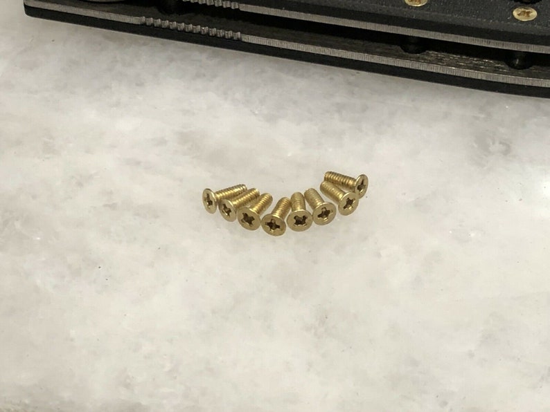 May include: A close-up of ten gold-colored screws with a cross-shaped head.