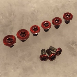 May include: A set of eight red screws, some with a star-shaped head and others with a flat head.