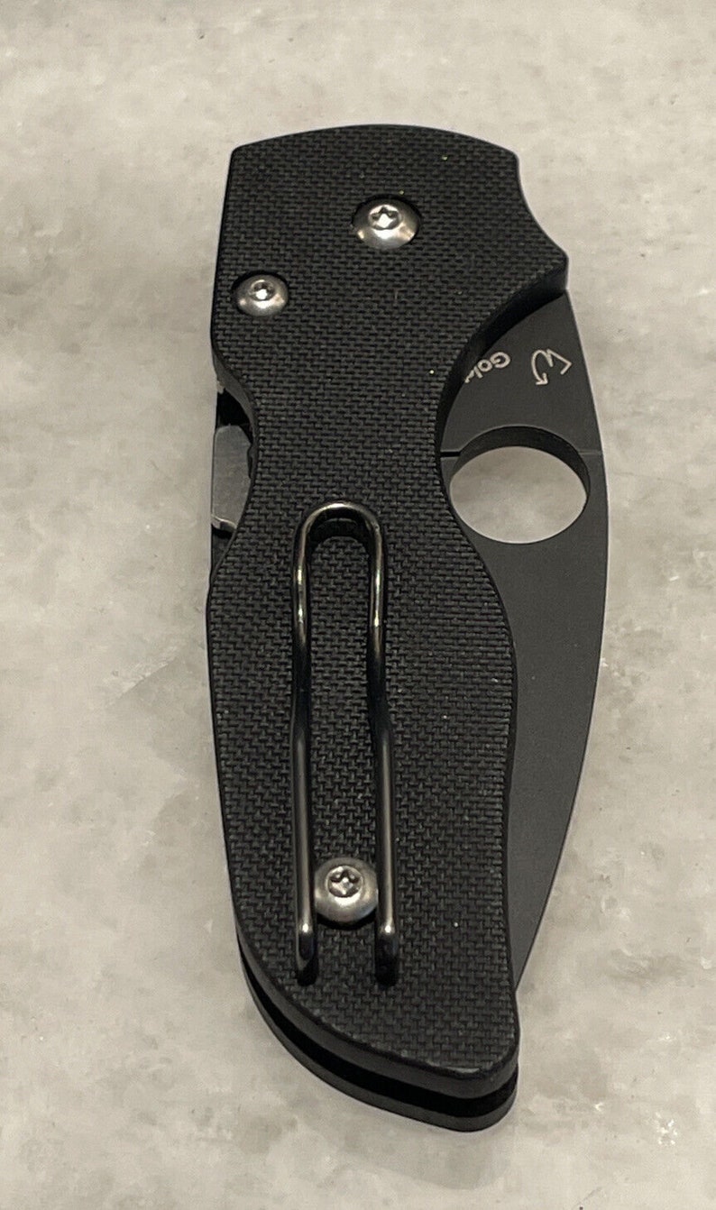 K&ouml;nnte beinhalten: Schwarzes Taschenmesser mit strukturiertem Griff und einem Clip. Das Messer hat ein kleines Loch an der Seite f&uuml;r eine Schnur.