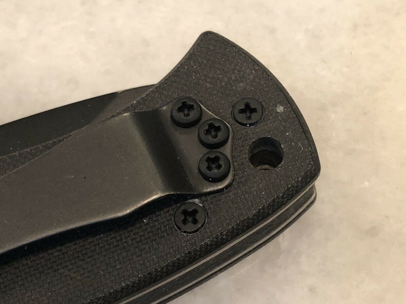 May include: Close-up of a black pocket knife with a clip and four black screws.