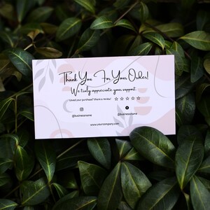 May include: A pink and white thank you card with a handwritten message that says "Thank You For Your Order! We truly appreciate your support." The card has a decorative design with abstract shapes and leaves. It also includes a five-star rating system and social media handles.