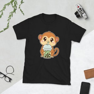 Puede incluir: Camiseta negra con un mono de dibujos animados que lleva un sombrero marrón y bebe un té de burbujas verde con boba negra.