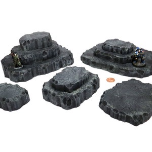 Puede incluir: Conjunto de seis plataformas de juego de mesa de color gris y textura de roca. Las plataformas son de varios tamaños y formas, algunas están apiladas unas sobre otras.