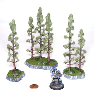 May include: Four miniature green pine trees on bases with a gray rock texture. The trees are made of green flocking and have brown branches. The bases are covered in green flocking and have small gray rocks. A miniature space marine figure stands in front of the trees.