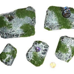 May include: Five different sized, gray and green, rocky terrain pieces for tabletop gaming. The pieces are made of foam and have a realistic texture.