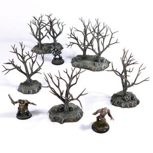 May include: Six miniature bare trees on grey bases, with two miniature figures in the foreground. The trees are made of brown branches and are arranged in a circle.