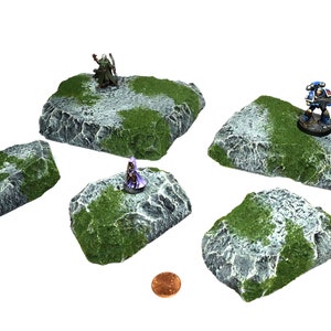 Puede incluir: Cinco bases de terreno rocoso grises y blancas con hierba verde y figuras en miniatura. Las bases están diseñadas para juegos de mesa.