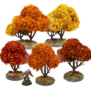 May include: A collection of five miniature model trees with autumn foliage in shades of orange, yellow, and red, each mounted on a circular base with green ground texture, accompanied by a small brown figurine of a bipedal creature.