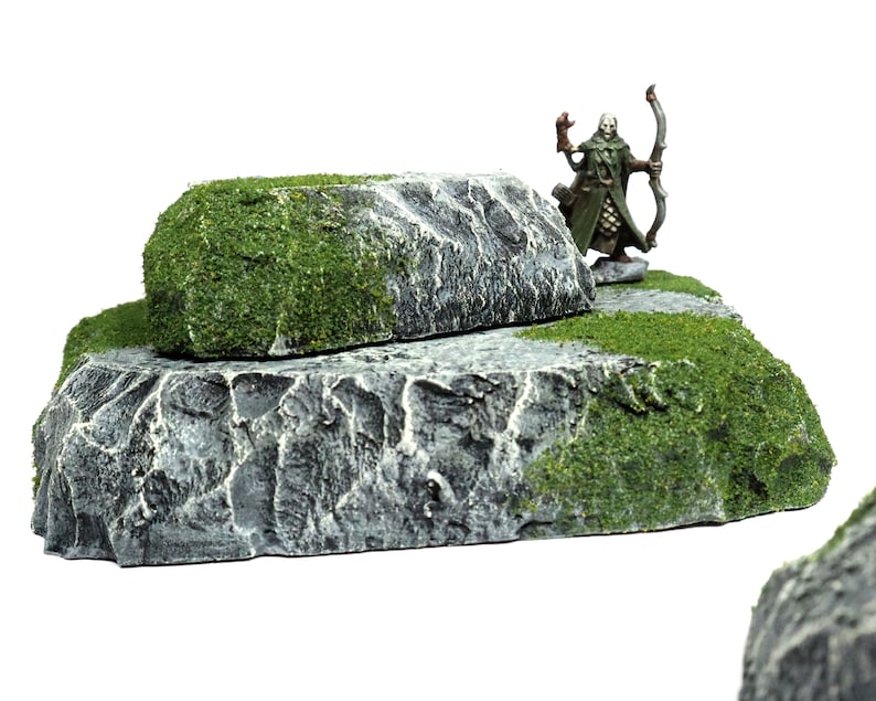 May include: A miniature figure of an elf archer standing on a two-tiered rock formation. The rock is painted gray with green moss accents.