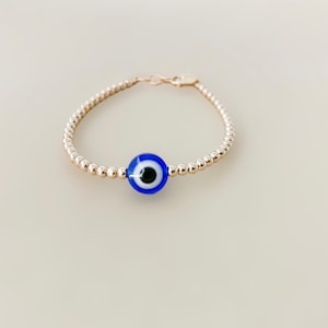 May include: A gold beaded bracelet with a blue evil eye charm.