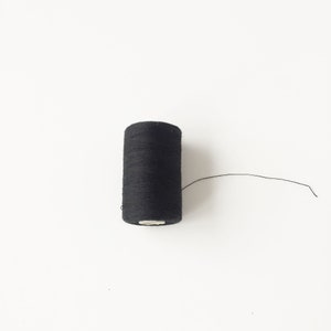 May include: A spool of black thread with a small amount of thread extending from the spool.