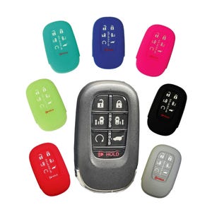 May include: Assortment of silicone key covers in various colors, including green, blue, pink, black, red, and gray. The covers are designed to fit a car key fob with multiple buttons, including a hold button. The key fob has a silver metal casing.