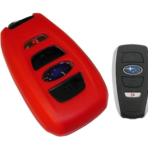 May include: Red silicone key fob cover for a Subaru car key. The key fob has four buttons and a Subaru logo. The key fob is next to a silver and black Subaru car key.