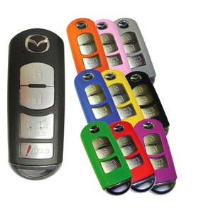 May include: A black car key with a Mazda logo and four buttons. The key is surrounded by nine colorful silicone key covers in orange, pink, gray, blue, yellow, black, green, red, and purple.