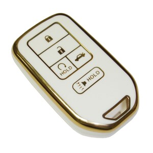 May include: White car key fob with gold trim and buttons. The buttons are labeled "Hold" and have icons for lock, unlock, trunk, and panic.