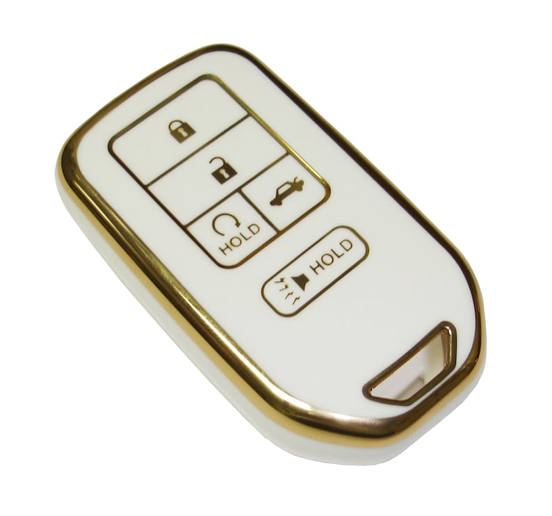 May include: White car key fob with gold trim and buttons. The buttons are labeled "Hold" and have icons for lock, unlock, trunk, and panic.