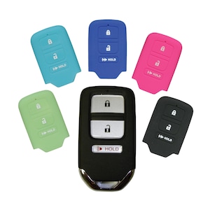 May include: Five silicone key covers for a car key fob. The covers are in different colors: light blue, green, pink, black, and blue. The key fob has three buttons: lock, unlock, and hold. The key fob is black with silver buttons.