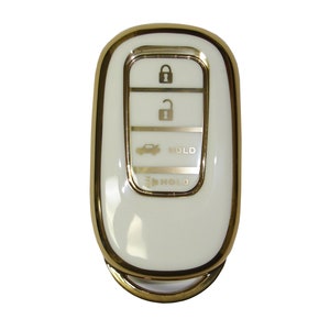 May include: A white car key fob with a gold trim. The key fob has four buttons: lock, unlock, trunk, and panic. The buttons are labeled with icons. The key fob also has a gold ring.