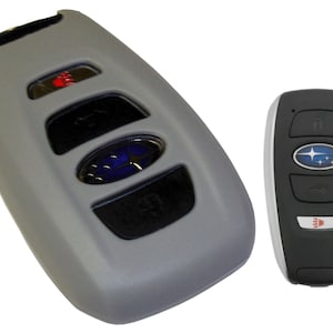 May include: Two gray car key fobs with a Subaru logo. The key fob on the left has four buttons and a red button. The key fob on the right has three buttons and a red button.