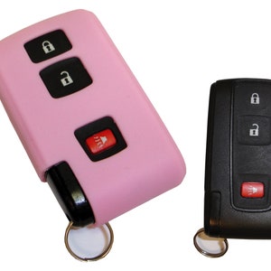 May include: A pink silicone key fob cover for a car key with three buttons, including lock, unlock, and panic. The key fob has a silver key ring attached.
