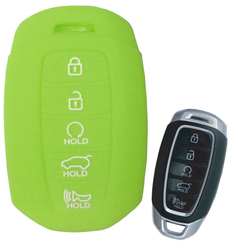 Puede incluir: Funda de silicona verde para llavero con botones blancos etiquetados como "HOLD" para una llave de coche con un mando a distancia negro. El mando a distancia tiene detalles plateados y botones etiquetados como "HOLD".