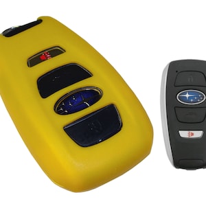 May include: Yellow silicone key fob cover for a Subaru car key. The cover has four buttons and a Subaru logo. The key fob is black with a silver trim and a Subaru logo.
