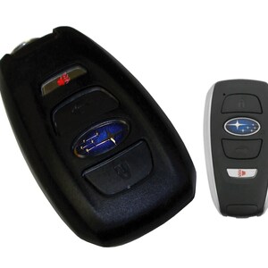 May include: Two black car key fobs with a silver Subaru logo and buttons for lock, unlock, trunk, and panic. The key fob on the left has a red LED light.