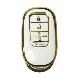 May include: A white car key fob with a gold trim. The key fob has five buttons: lock, unlock, trunk release, panic, and hold.