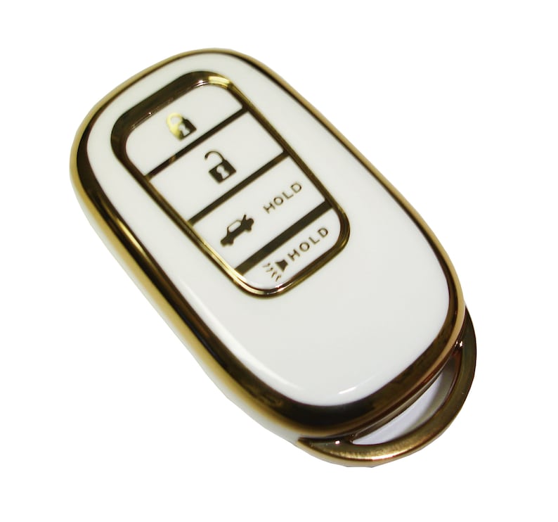 May include: White car key fob with a gold trim. The key fob has four buttons: unlock, lock, trunk release, and panic. The buttons are labeled with the words "HOLD".