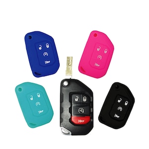 May include: A collection of car key fobs and protective silicone covers in various colors. The key fobs are black with silver accents and red buttons. The silicone covers are blue, pink, teal, and black, each with matching button icons.