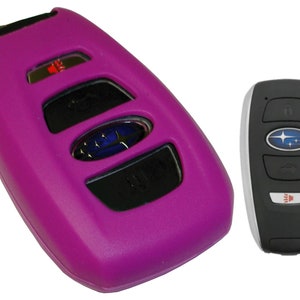 May include: A purple silicone key fob cover for a Subaru car key. The key fob has four buttons and a Subaru logo.