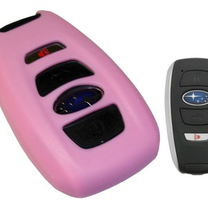 May include: Pink silicone key fob cover for a Subaru car key. The cover has a cutout for the Subaru logo and buttons. The key fob is black with a silver trim.