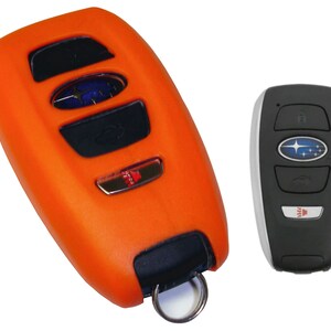 May include: Orange silicone key fob cover for a Subaru car key. The key fob has four buttons and a Subaru logo. The key fob is attached to a silver key ring.
