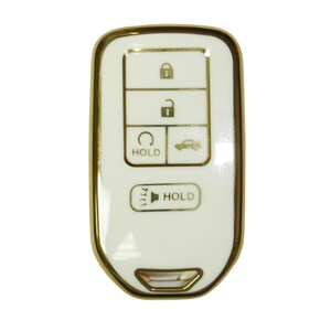 May include: A white car key fob with a gold trim. The key fob has five buttons: lock, unlock, trunk release, panic, and a button with a car icon and the word "HOLD".