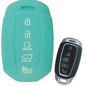 Puede incluir: Una funda de silicona para llave de coche de color turquesa con cinco botones. Los botones tienen iconos blancos para bloquear, desbloquear, maletero, p&aacute;nico y mantener. La funda se muestra junto a una llave de coche negra con los mismos iconos.