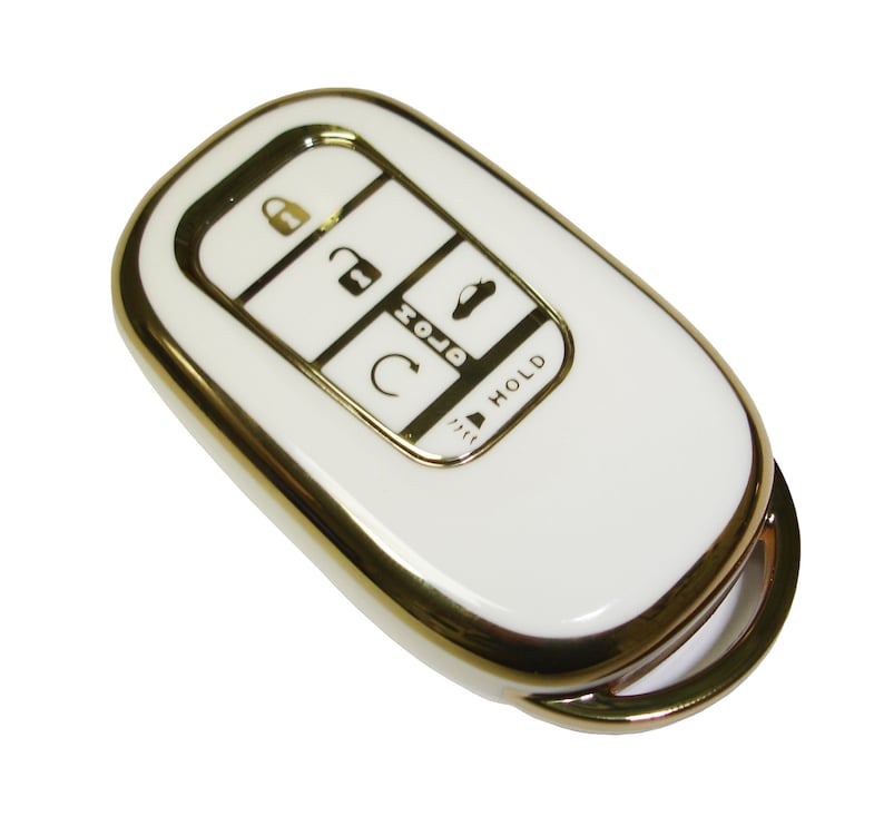 May include: White car key fob with a gold trim. The key fob has five buttons: lock, unlock, trunk, panic, and hold.