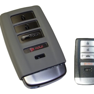 May include: Two car key fobs, one gray and one black, with four buttons each. The gray fob has a red "HOLD" button. Both fobs have a silver trim.