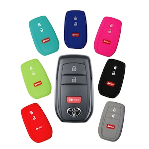 May include: A collection of car key fobs, including a central black Toyota key and several silicone covers in various colors: teal, blue, pink, green, red, black, and gray. Each cover has the word "HOLD" printed on it.
