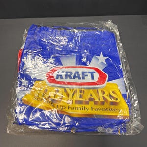 May include: A blue and white Kraft tote bag with a star pattern. The bag features the Kraft logo in a red and white oval, with the words "100 YEARS" in gold lettering. The text "Serving Up Family Favorites" is also visible.