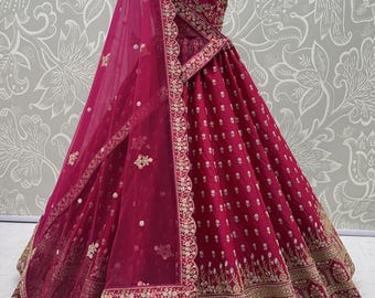 May include: A magenta lehenga choli set featuring a sleeveless blouse and a voluminous floor-length skirt. Both pieces are adorned with intricate gold embroidery and small floral motifs. A matching sheer magenta dupatta with a scalloped border.