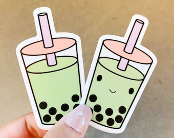 May include: Two green bubble tea stickers with pink straws and white outlines. The bubble tea on the right has a smiling face.