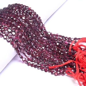 Peut inclure: Un brin de perles de pierres précieuses rouge foncé, chaque perle ayant une forme de larme. Les perles sont enfilées sur un cordon rouge et ont un pompon rouge à l'extrémité.