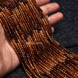 May include: A strand of brown and orange gemstone beads. The beads are faceted and have a slightly irregular shape. The beads are strung on a clear thread and are approximately 4mm in diameter.