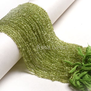 Puede incluir: Una hebra de cuentas de peridoto verde claro, de aproximadamente 2 mm de diámetro, con un borla verde en el extremo. Las cuentas son facetadas y tienen un aspecto brillante y translúcido.