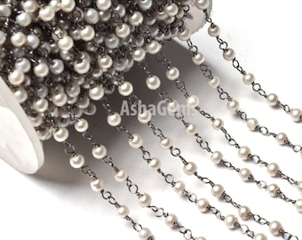 Op de afbeelding: Een spoel met witte parel- en zilveren ketting, de ketting is een delicate kabelketting met kleine ronde parels die eraan geregen zijn. De ketting is perfect voor het maken van sieraden.