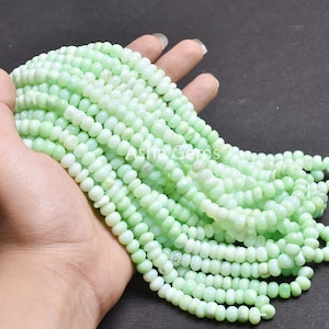 May include: A collection of light green, round gemstone beads. The beads are strung together, creating multiple strands. The beads have a smooth, polished surface and are of a consistent size. The overall colour is a soft, pastel green.