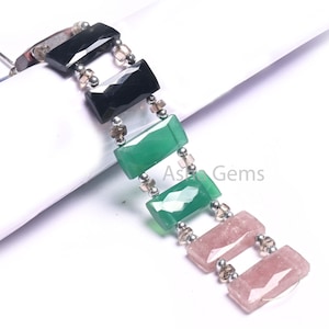 Puede incluir: Un brazalete hecho con cuentas rectangulares de piedras preciosas negras, verdes y rosas separadas por cuentas espaciadoras plateadas y marrones.