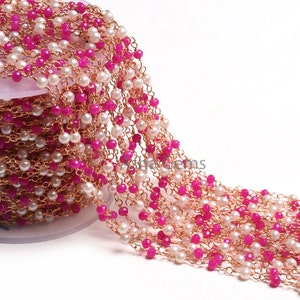 May include: A strand of pink and white beads with a gold chain. The beads are faceted and the chain is delicate. The strand is coiled on a white spool.